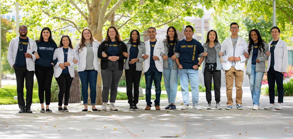 Students wearing a blue T-shirt with the words “UC Davis School of Medicine” stands in front of the school’s Education Building